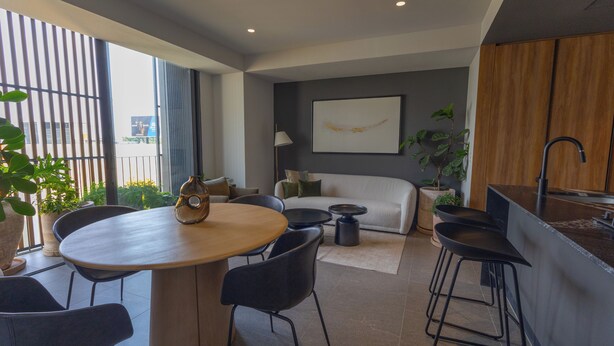 Un espacio habitable moderno con comedor, sofá, cocina con pileta y un amplio ventanal con persianas.
