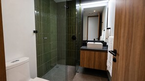 Ein modernes Badezimmer mit einer in Glas abgeschirmten Dusche, einem hölzernen Waschtisch und einer weißen Toilette.
