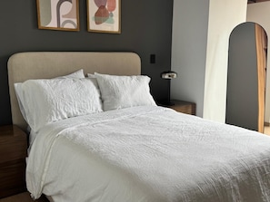 Ein Bett mit beigem Kopfteil, weißer Bettwäsche und zwei abstrakten Bildern an der Wand.