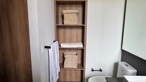 Un baño moderno con tocador de madera, inodoro y estante con toallas dobladas.
