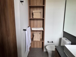 Ein modernes Badezimmer mit einem Holzlagerflächezettel, einer Toilette und einem Regal mit gefalteten Handtüchern.
