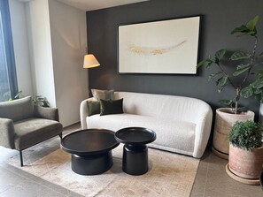 Ein modernes Wohnzimmer mit einer Couch, zwei schwarzen Couchtischen, einer Lampe und einem großen abstrakten Gemälde an der Wand.