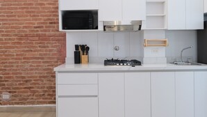 Cocina moderna con muebles blancos, pared de ladrillo, microondas, estufa a gas y un utensilio de madera.