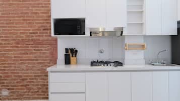 A modern kitchen with white cabinetry, a brick wall, a microwave, a gas stove, and a wooden utensil holder.