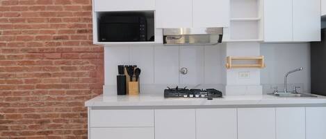 Een moderne keuken met witte kastjes, een bakstenen muur, een magnetron, een gasfornuis en een houten snoerhouder.