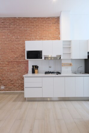 A modern kitchen with white cabinetry, a brick wall, a microwave, a gas stove, and a wooden utensil holder. - Casa Franco - Live in the Old Town (Panamá)