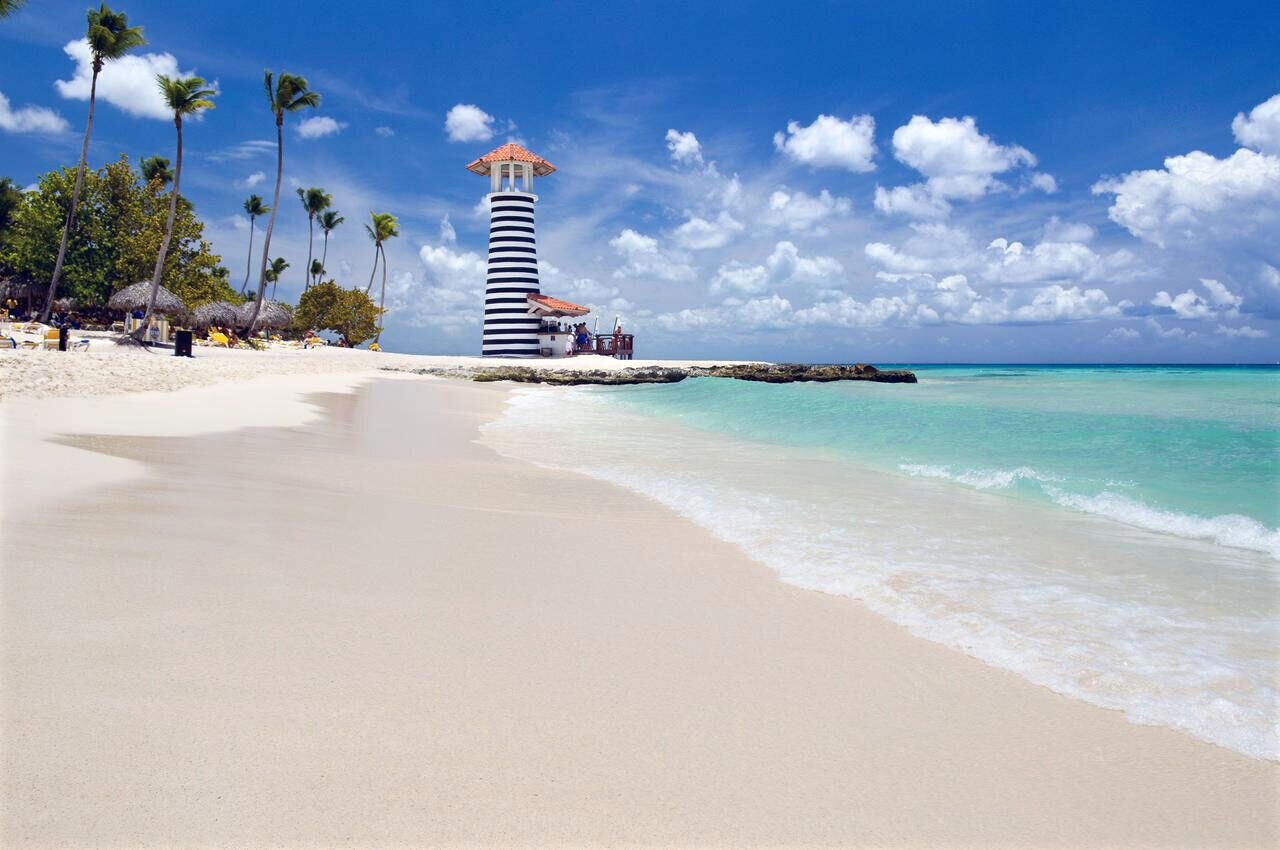 A beach with a lighthouse, palm trees, and clear turquoise waters.