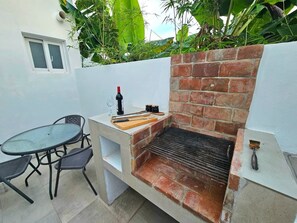 An outdoor patio with a brick grill, a table with chairs, and a small window.