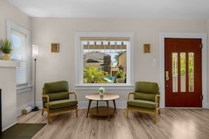 A room with two green armchairs, a small round table, a red door, and a window with a view of buildings and greenery. - Mission Hills retreat, walkable, free parking (San Diego)
