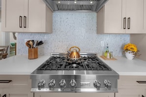 A kitchen with a stainless steel ZLINE gas stove, wooden utensils in a holder, and a vase with yellow flowers on the counter. - Mission Hills retreat, walkable, free parking (San Diego)