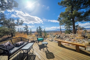 Eine Holzterrasse mit einer Couch, Stühlen und einer Bank, mit Blick auf eine Berglandschaft.