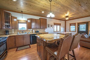 A kitchen with wooden cabinets, a central island, a dining area with a table and chairs, and a ceiling fan. - Ridgeview Haven-perfect retreat (Fairplay)