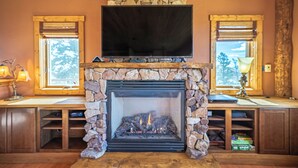 A fireplace with a stone surround, a flat-screen TV mounted above it, and a window on either side of the fireplace. - Ridgeview Haven-perfect retreat (Fairplay)