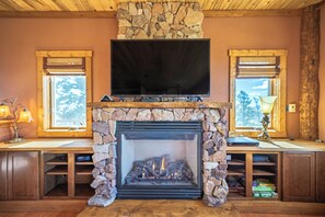 A fireplace with a stone surround, a flat-screen TV mounted above it, and a window on either side of the fireplace. - Ridgeview Haven-perfect retreat (Fairplay)