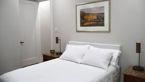 A bedroom with a bed, a nightstand, a bedside table, a framed painting, and a door. - Stylish 4BR Near Hobby, Med Center, NRG & Downtown (Houston)