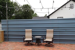 A patio with two chairs and a small table, a blue metal wall, and string lights. - Stylish 4BR Near Hobby, Med Center, NRG & Downtown (Houston)