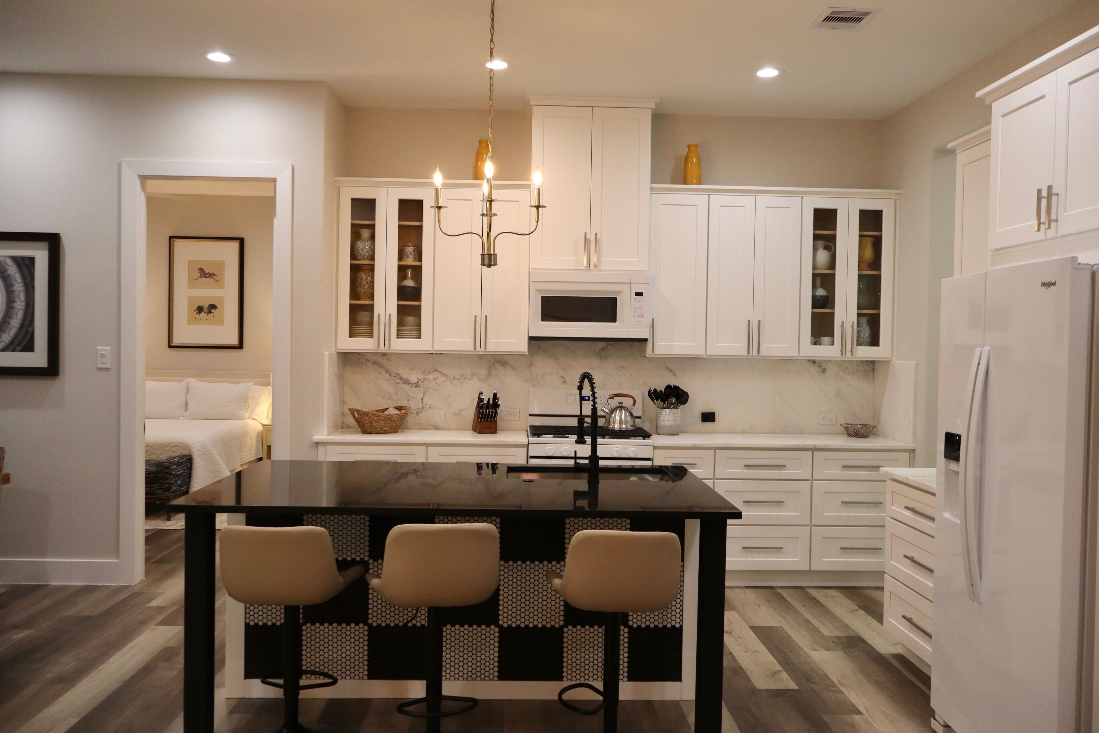 A modern kitchen with white cabinetry, a central island with bar stools, a built-in microwave, and a refrigerator.