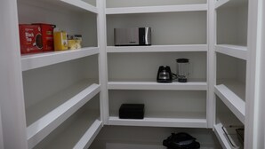 A white storage unit with shelves, containing a coffee maker, a blender, and boxes of tea. - Stylish 4BR Near Hobby, Med Center, NRG & Downtown (Houston)