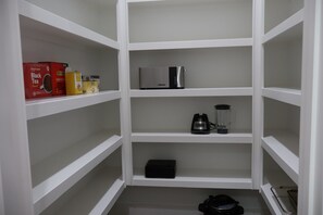 En vit förvaringsenhet med hyllor som innehåller olika föremål, bland annat en kaffebryggare, en mixer och teförpackningar.