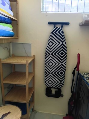 Ein Zimmer mit einer Holzhockerreih, einem gemusterten Bügelbrett und einem Staubsauger.