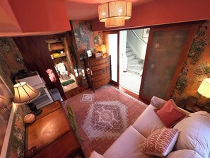 Quarto com cama, penteadeira, luminária e janela com vista para uma escada.