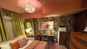 Ein Schlafzimmer mit Bett, Schreibtisch, Stuhl, Kommode und einer Wand mit Blumenmuster.