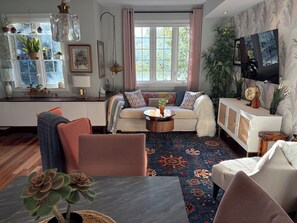 A living room with a sofa, coffee table, and chairs, a television, and a window with curtains.