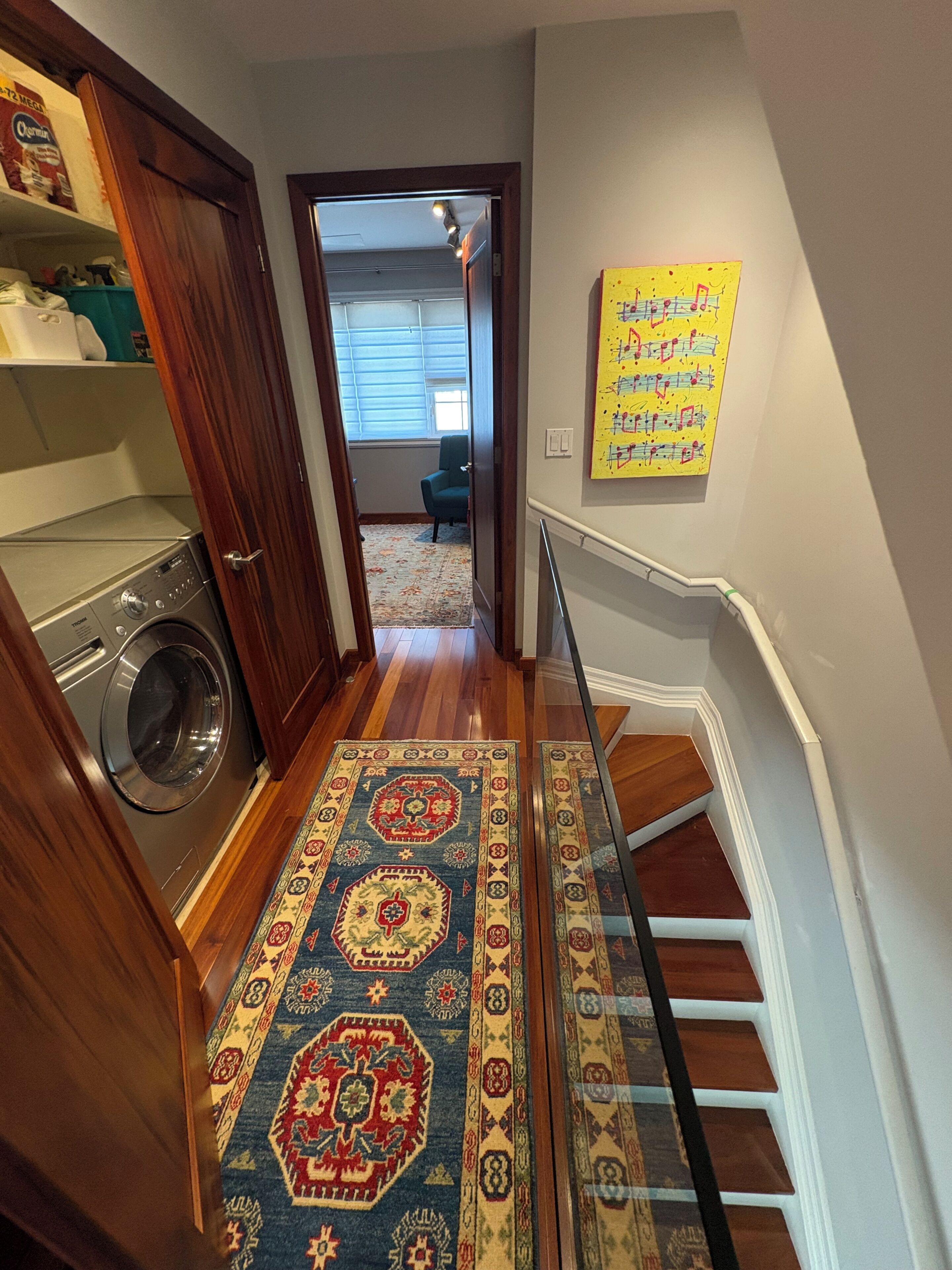 A hallway with a washing machine, a patterned rug, and a staircase with a handrail.