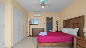 Ein Hotelzimmer mit Bett, Nachttisch, Deckenventilator und Blick ins Badezimmer.