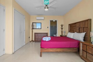 Ein Hotelzimmer mit Bett, Nachttisch, Deckenventilator und Blick ins Badezimmer.