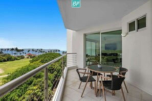 A balcony with a table and chairs, a view of a lush green landscape, and a clear blue sky. - Beachfront 2BR w/ Partial Ocean View + Resort Pools (Nuevo Nayarit)