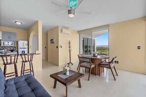 A modern living room with a sofa, a coffee table, and a dining area with chairs and a table. - Beachfront 2BR w/ Partial Ocean View + Resort Pools (Nuevo Nayarit)