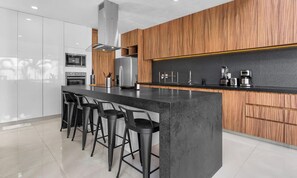 A modern kitchen with a central island, bar stools, wooden cabinetry, and stainless steel appliances. - 4BR Villa with Private Pool, Jacuzzi + Beach Club (Cruz de Huanacaxtle)