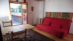 A room with a wooden dining table, a red sofa, a patterned rug, and a view through a glass door. - 2 bedroom building in Hechingen with pool, balcony, terrace  for relaxing stay (Hechingen)