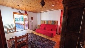 A room with a wooden ceiling, a red sofa, a patterned rug, a dining table with chairs, and a view through a door. - 2 bedroom building in Hechingen with pool, balcony, terrace  for relaxing stay (Hechingen)