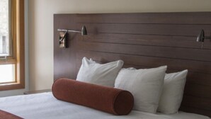 Ett hotellrum med en stor säng, en sänggavel i trä och två vägglampor.
