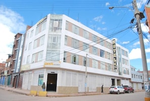 Un edificio de hotel de varios pisos con un cartel llamativo, una entrada a nivel de calle y un área de estacionamiento visible.