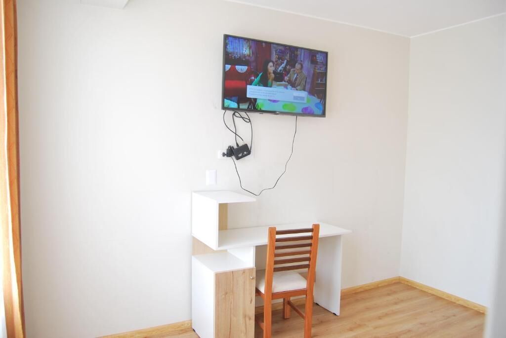 Une pièce avec un bureau blanc, une chaise en bois et un téléviseur fixé au mur.