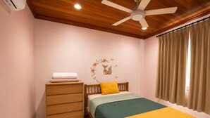 A bedroom with a bed, a wooden dresser, a ceiling fan, and a window with curtains.
