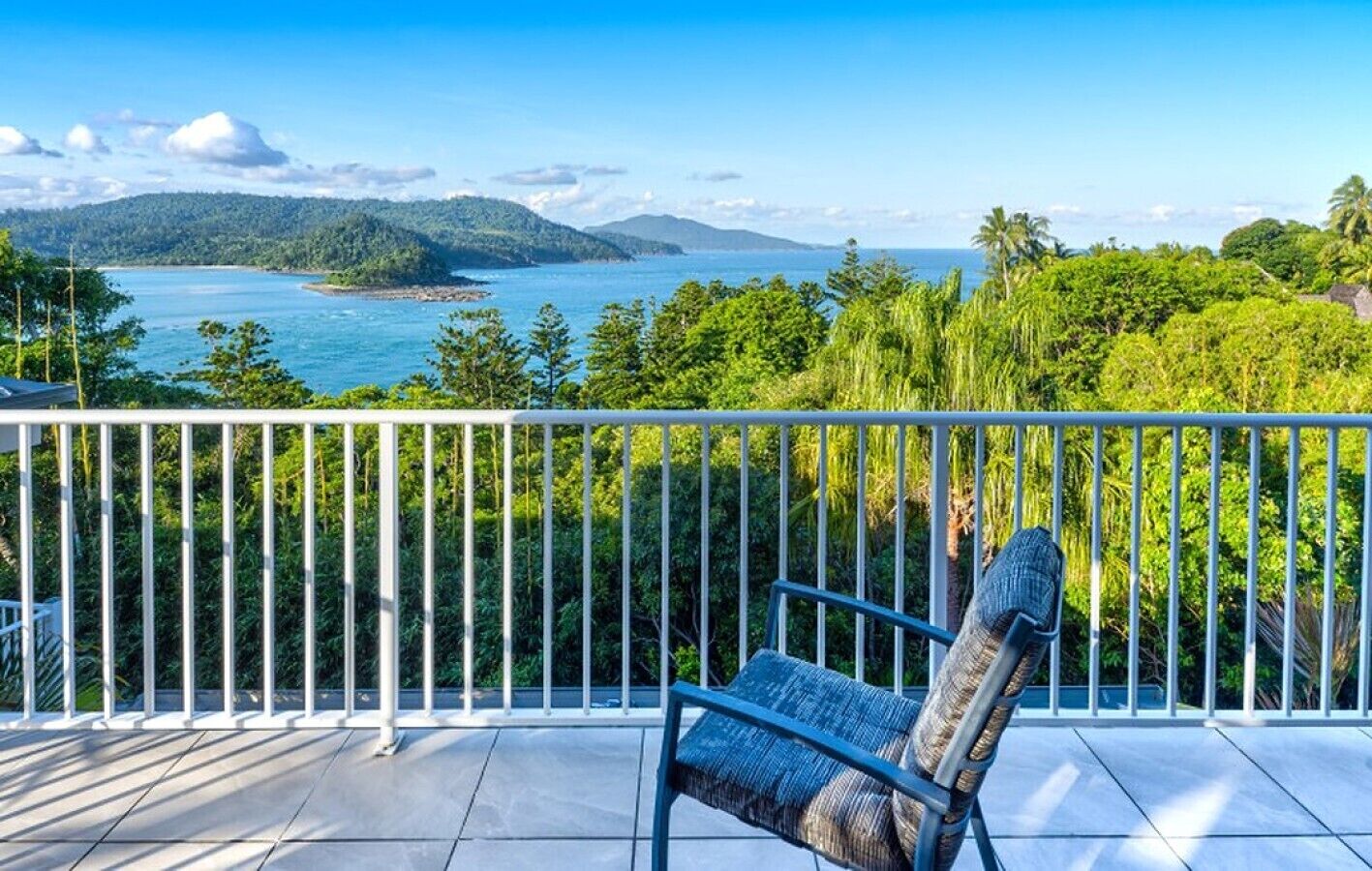 A balcony with a view of a coastal landscape, including a body of water and distant mountains.