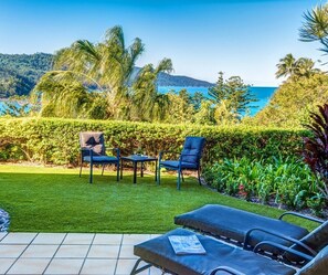 A patio with outdoor furniture, a view of the sea, and a well-maintained garden.
