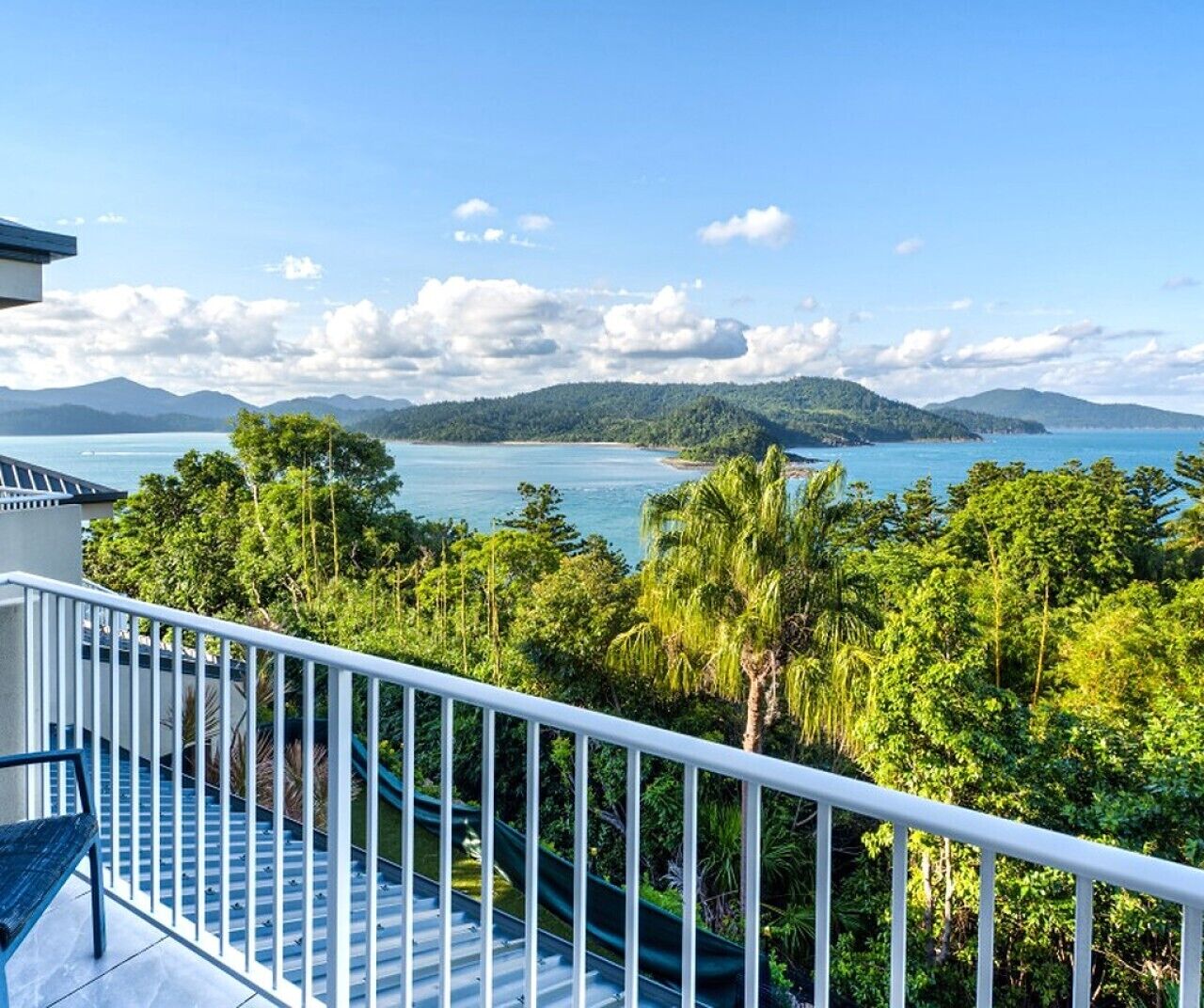 Un balcon offrant une vue sur un paysage côtier, comprenant une étendue d’eau, de la végétation et des montagnes au loin.