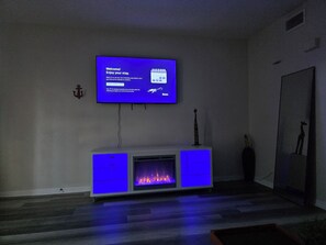 A living room with a flat-screen TV mounted on the wall, a fireplace, and a small statue on the mantel. - Waterfront Canal Townhouse with Private Dock on the Island, Corpus Christi (Corpus Christi)