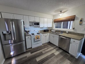 A modern kitchen with stainless steel appliances, white cabinetry, and a herringbone tile backsplash. - Waterfront Canal Townhouse with Private Dock on the Island, Corpus Christi (Corpus Christi)