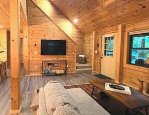 Ein Holzblock-Innenraum mit Fernseher, einer Couch, einem Couchtisch und einem Fenster mit Blick.
