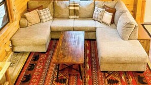 Interior acogedor de una cabaña de madera con un sofá modular, una mesa de centro y un tapete estampado.