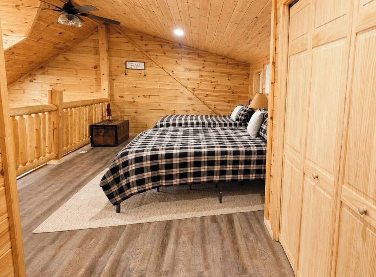 A wooden cabin bedroom with a bed, a nightstand, and a ceiling fan.