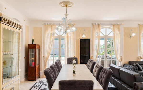 Ein Esszimmer mit einem langen Tisch, Stühlen, einer Kandelaber und Blick durch große Fenster.