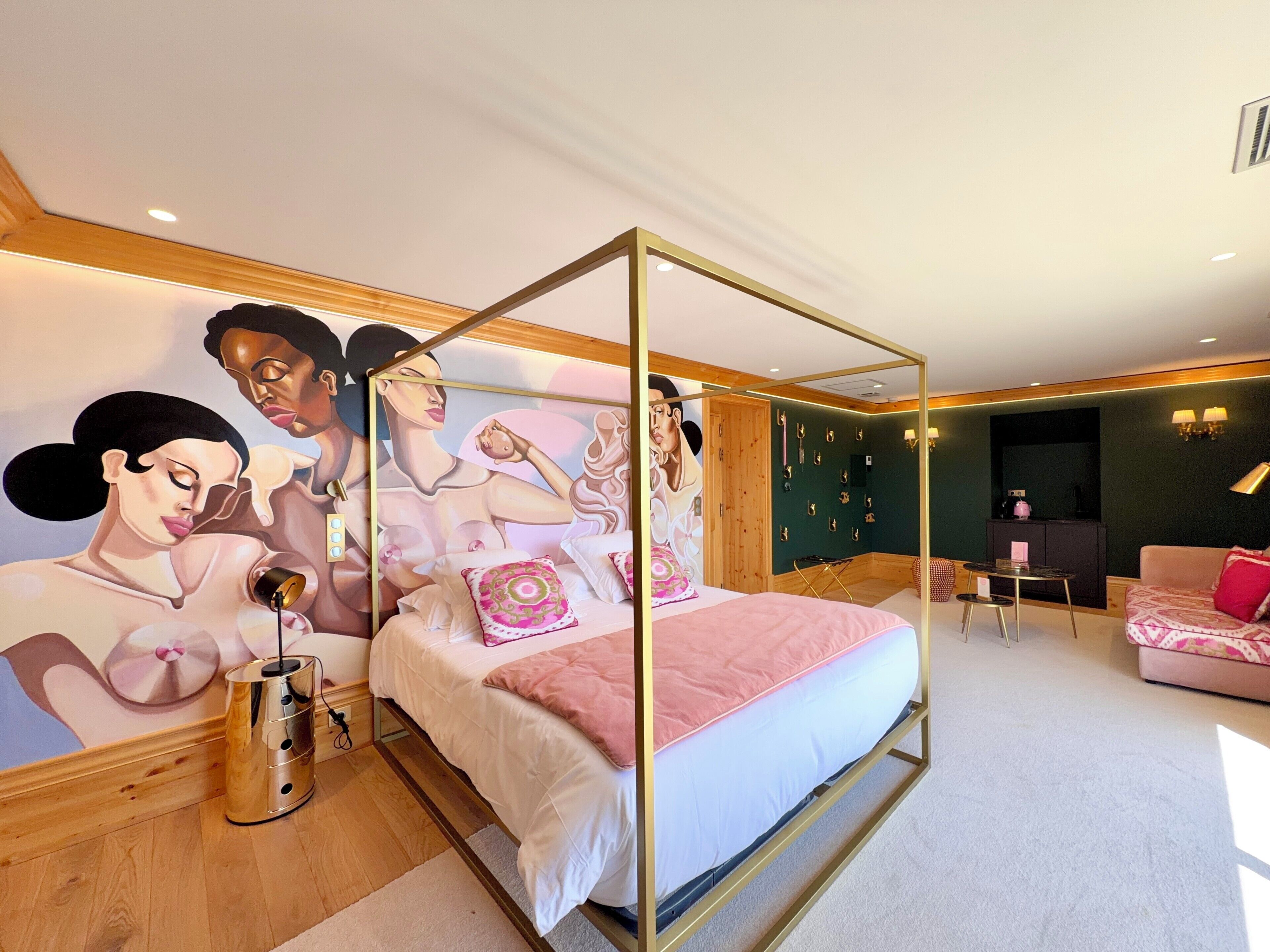 A bedroom with a four-poster bed, a large mural on the wall, and a seating area with a sofa and armchairs.