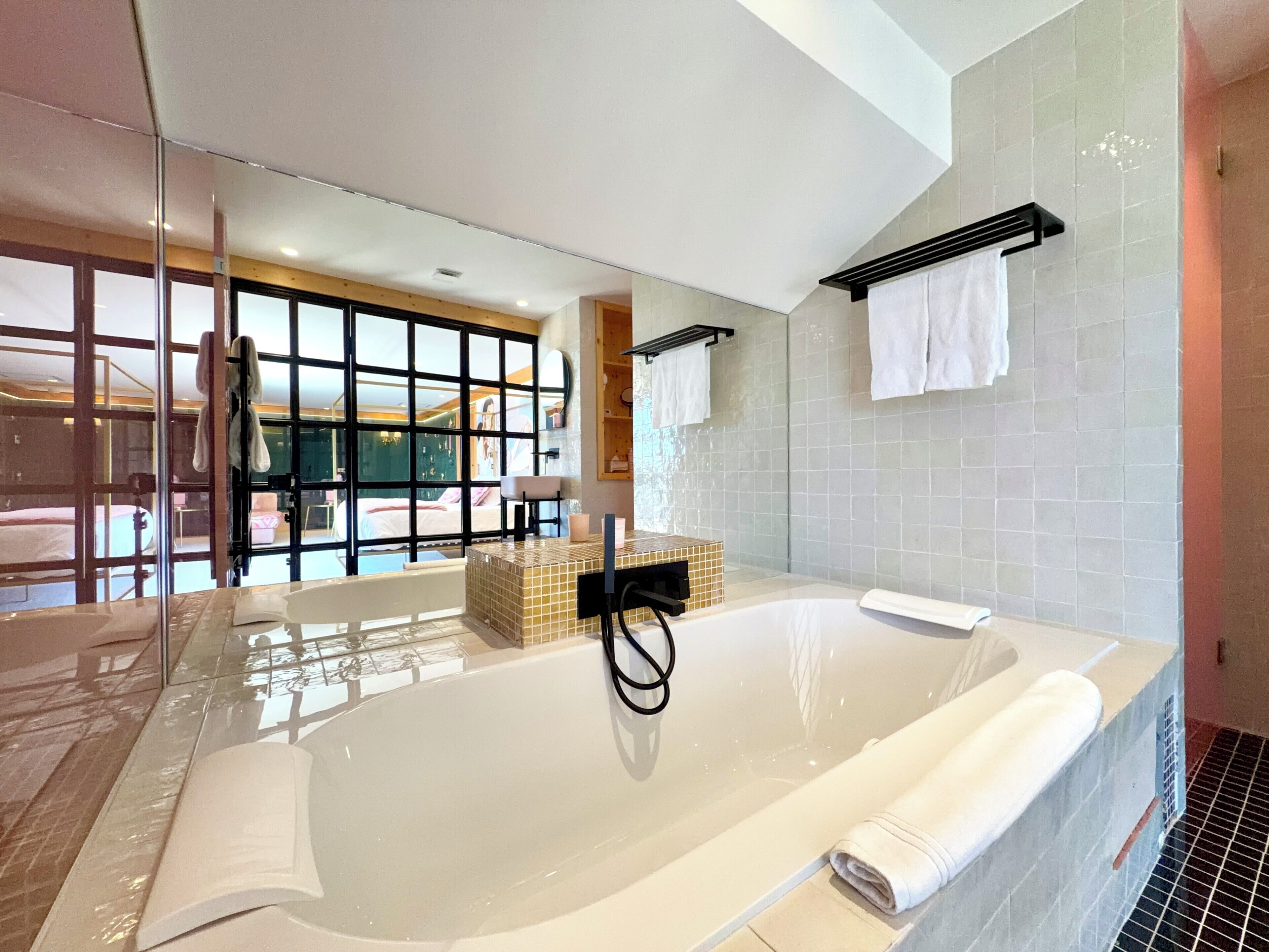 Une salle de bain moderne dotée d’une grande baignoire, d’une douche en verre et offrant une vue sur la chambre à coucher par le biais d’une grande fenêtre.